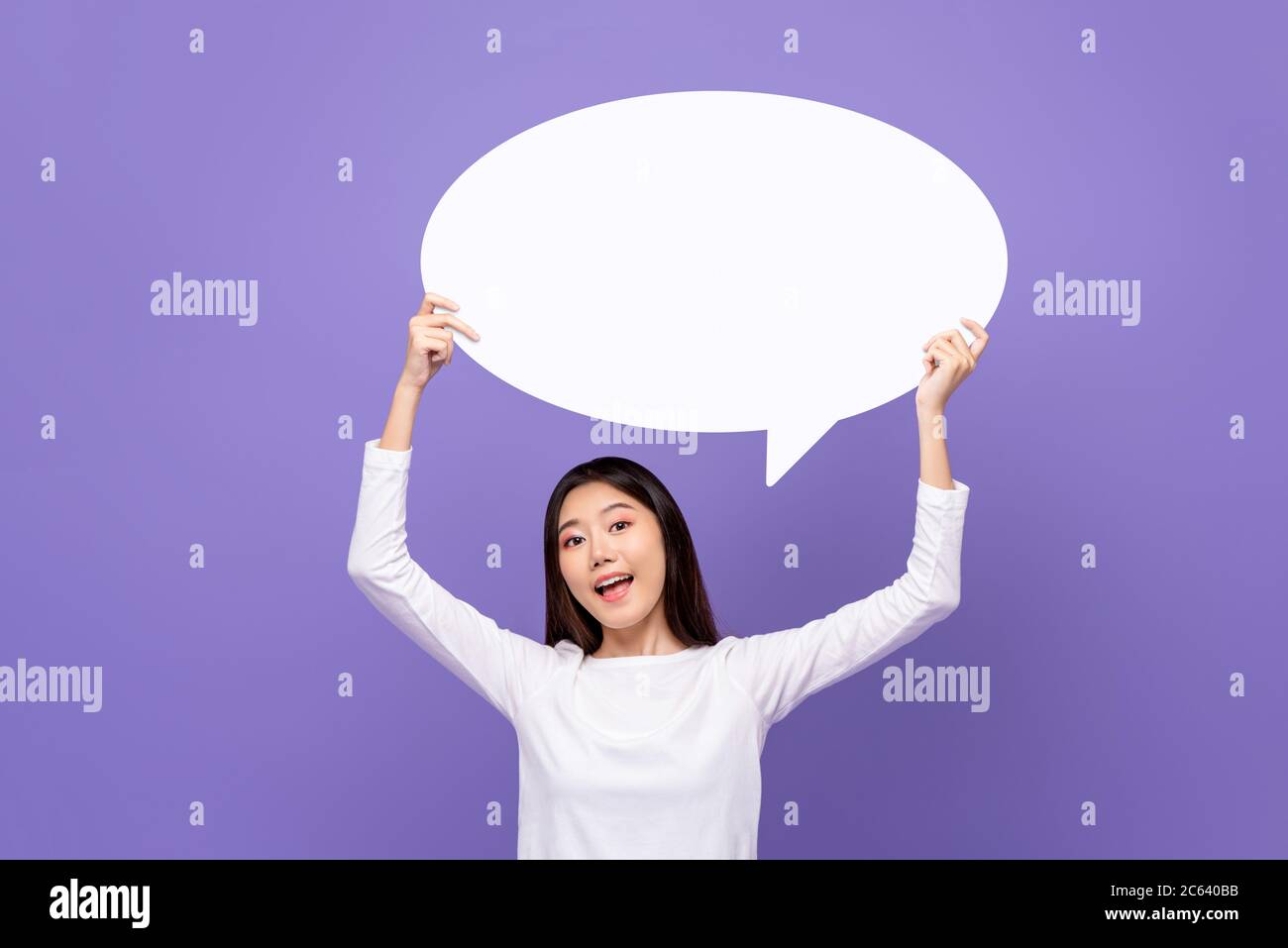 Beautiful Asian woman smiling and holding empty speech bubble isolated on purple background Stock Photo