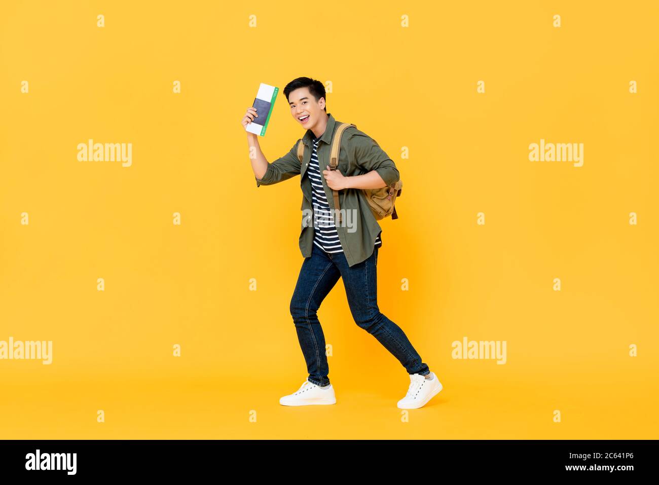 Young Asian man solo traveler with backpack passport and boarding pass ready to fly on isolated yellow background Stock Photo