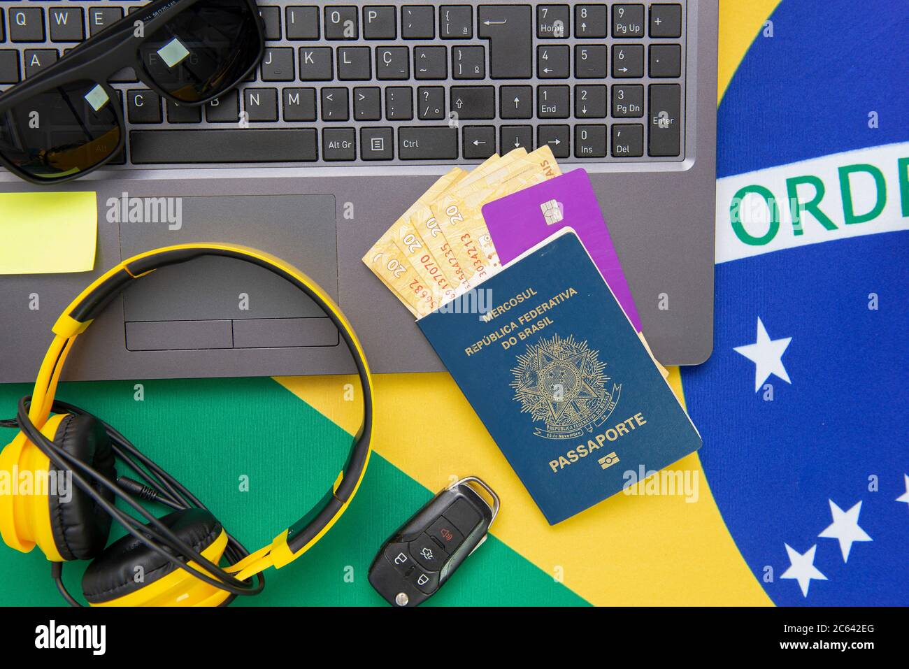 Top view of travel objects: Brazilian passport, notebook, sunglasses, keys, credit card, notepad, pen, money and Brazilian flag in the background. Tra Stock Photo