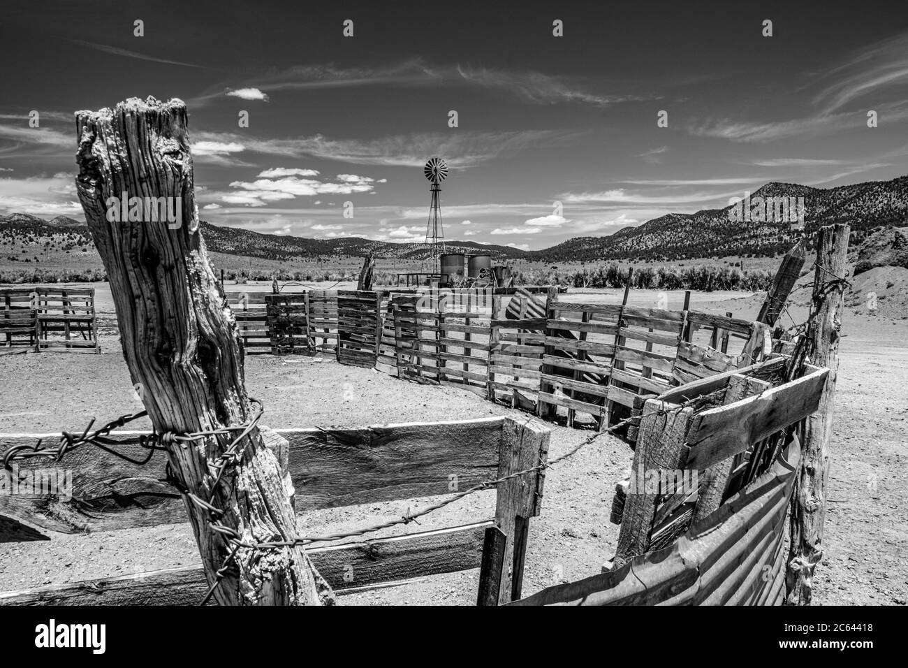 Black and White of an old western corral, windmill, and the blowing clouds. Stock Photo