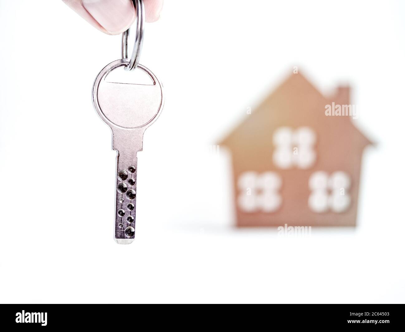 House loan and buying a property concept. Hand holding modern metal key with blank space on the key and miniature wooden house on white background. Stock Photo