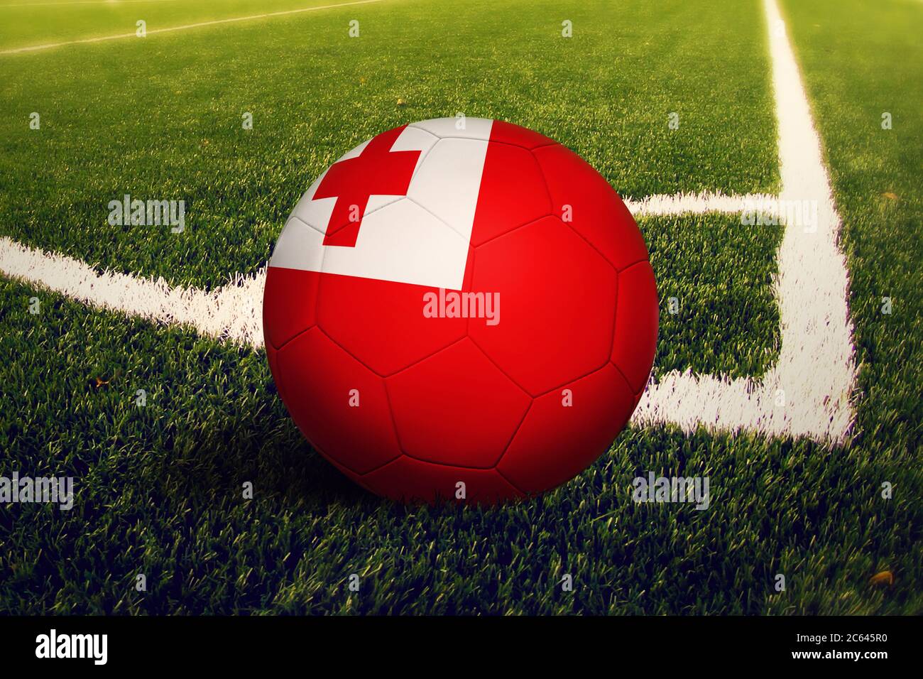 Tonga flag on ball at corner kick position, soccer field background. National football theme on green grass. Stock Photo