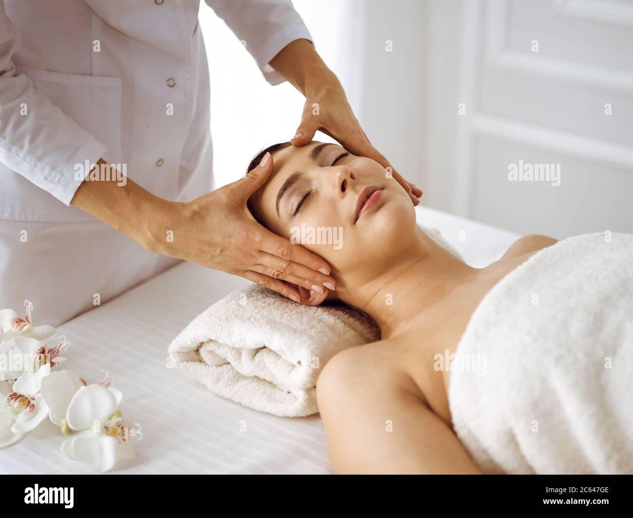 Beautiful brunette woman enjoying facial massage with closed eyes. Relaxing treatment in medicine and spa center concepts Stock Photo