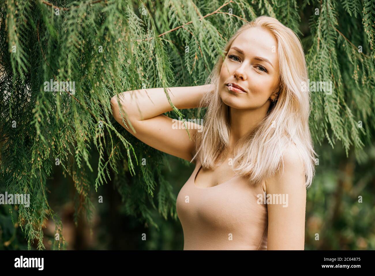 Caucasian young blonde woman standing beside tropical exotic plants. Botanic garden, rainforest, vacation and people concept. Beautiful lady wearing f Stock Photo