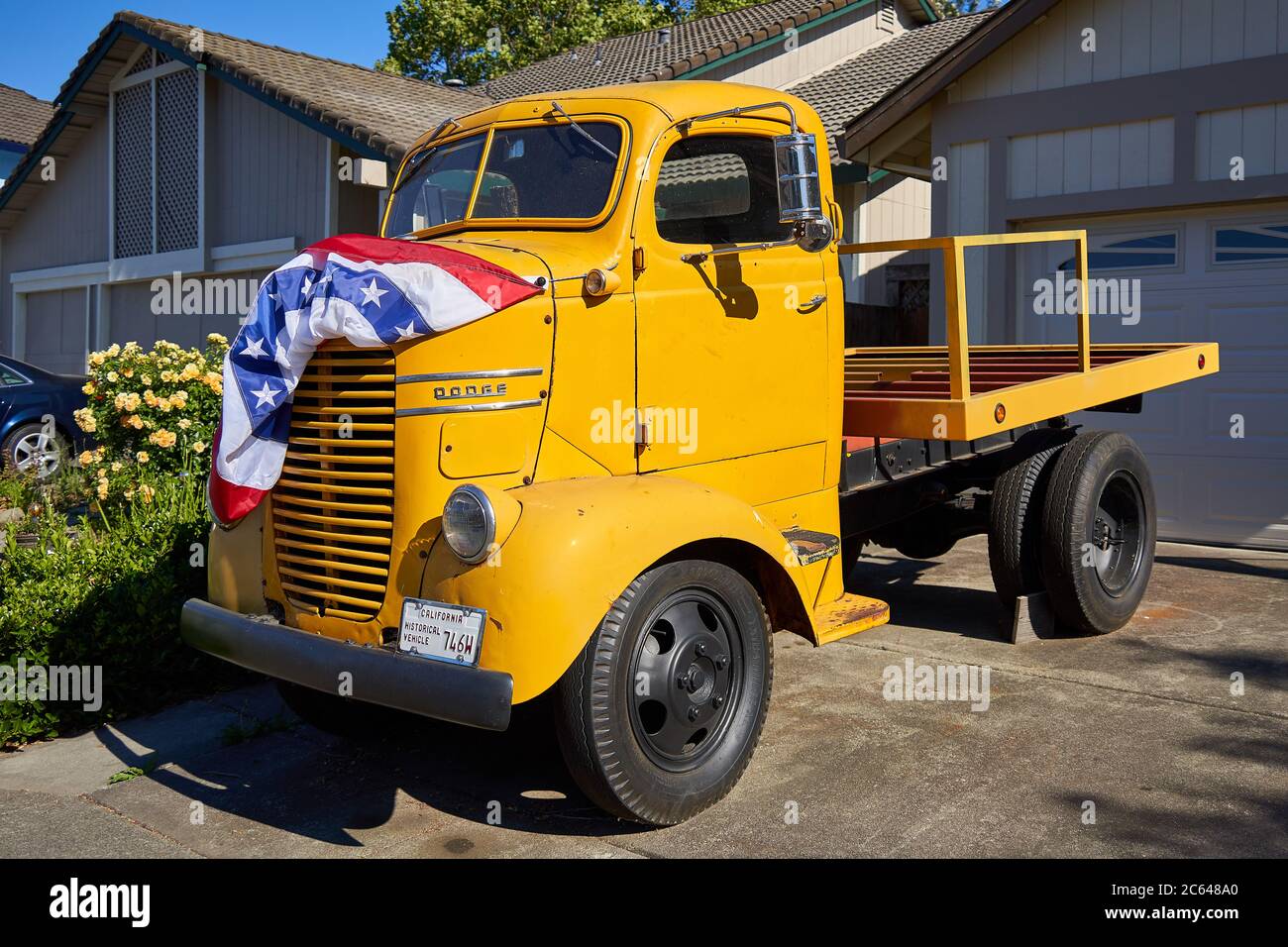 Classic Dodge truck with yellow exterior and American bunting flag on the hood. California Historical Vehicle in Windsor, California. Stock Photo
