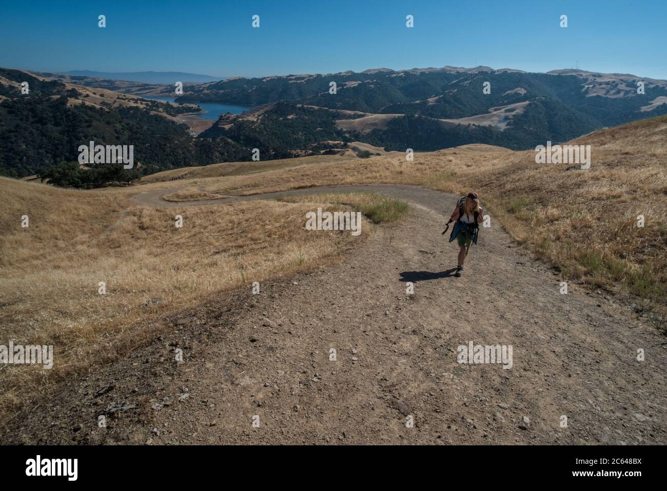 A single person walks uphill along a dirt road in Sunol wilderness in Alameda county, California. Stock Photo