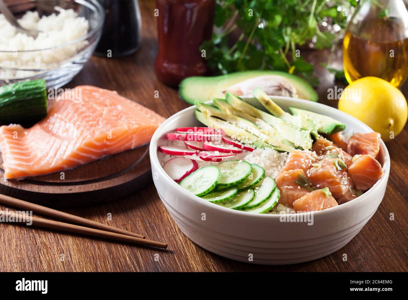 Poke bowl, traditional Hawaiian raw fish salad with rice, avocado, cucumber and radish on wooden background Stock Photo