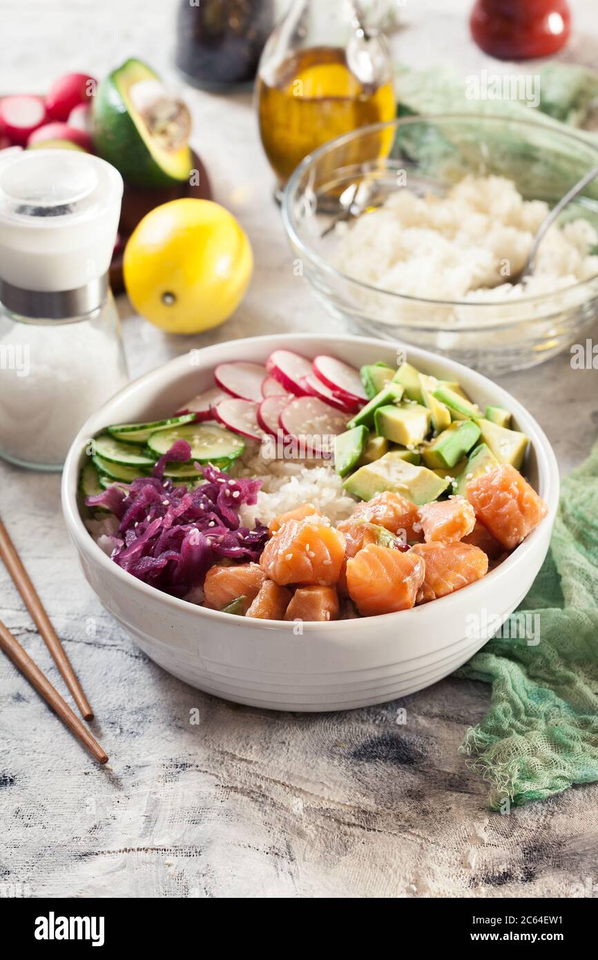 Poke bowl, traditional Hawaiian raw fish salad with rice, avocado, cucumber and radish on bright background Stock Photo