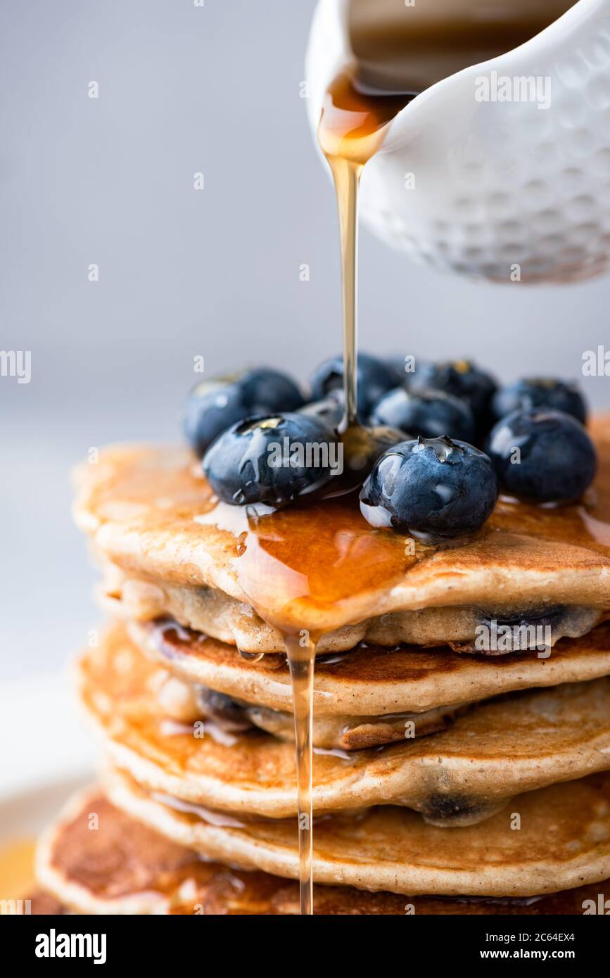 Maple syrup pouring on stack of pancakes closeup view. Sweet golden