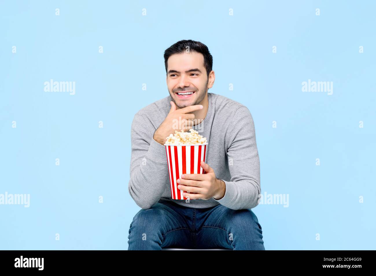 Laughing young man holding popcorn while watching movie isolated on light blue background Stock Photo