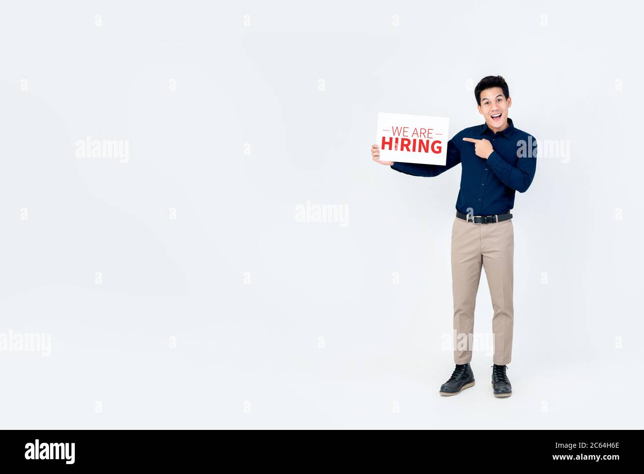 Portrait of smiling handsome Asian businessman holding and pointing to we are hiring sign in  isolated light gray background with copy space aside Stock Photo