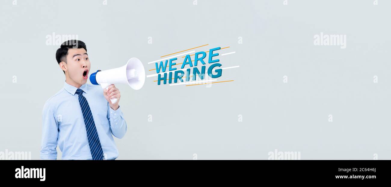 Panoramic portrait of young Asian businessman making announcement about job hiring with megaphone in isolated studio light gray background Stock Photo