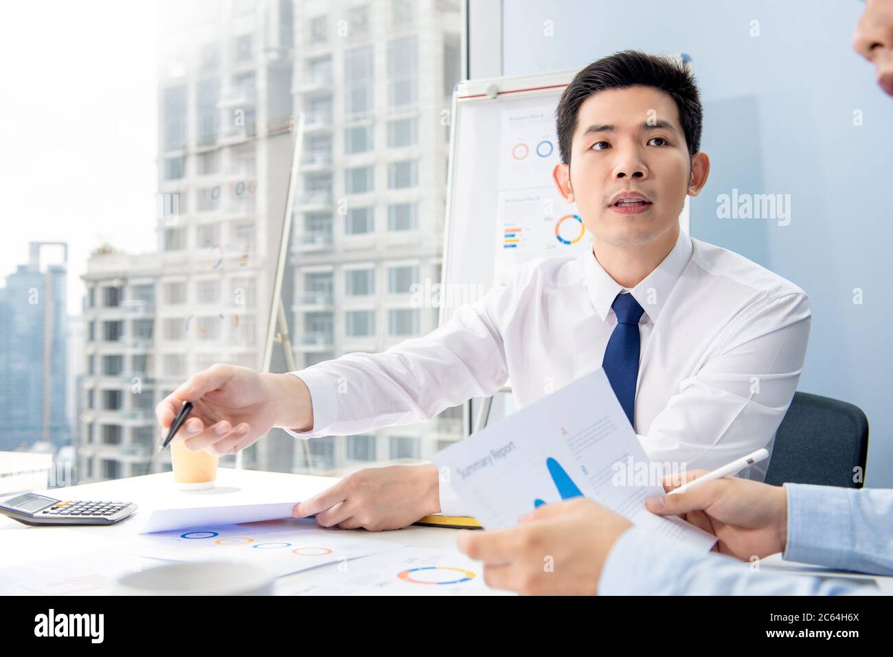Portrait of serious busy young Asian businessman analyzing data in an office meeting with colleague in urban setting Stock Photo