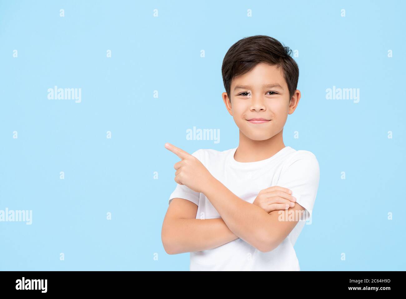 Close-up portrait of smiling young boy pointing finger on blank space beside in blue isolated background Stock Photo