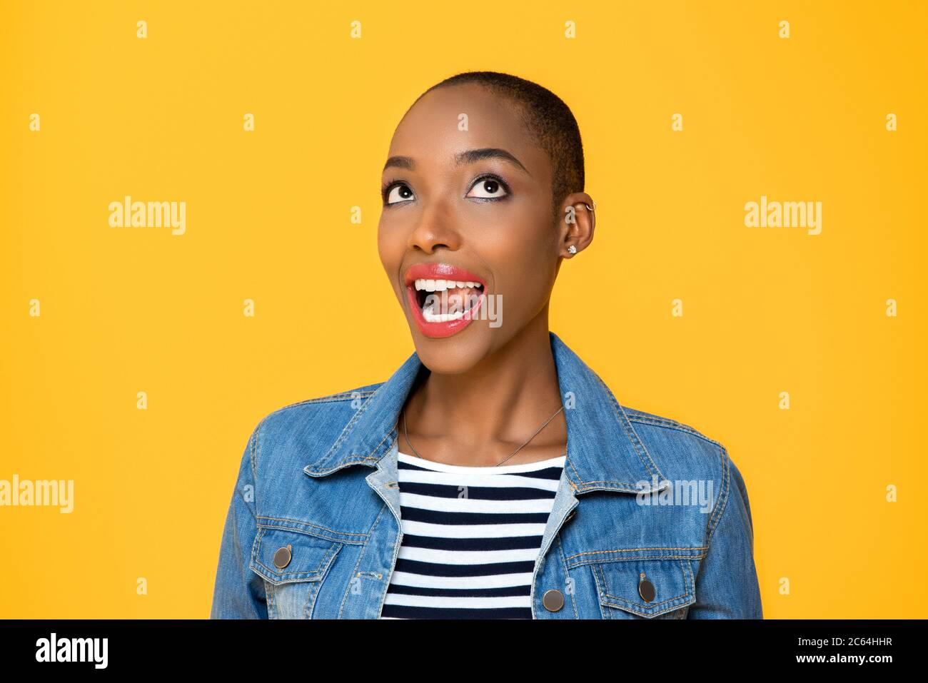 Close up portrait of happy young African American woman rolling her eyes looking up with mouth open in isolated studio yellow background Stock Photo