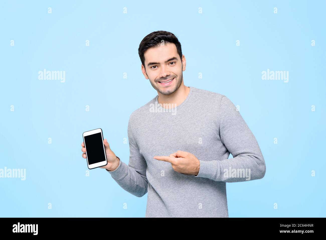 Portrait of smiling handsome Caucasian man holding and pointing finger to smart phone in isolated studio blue background Stock Photo