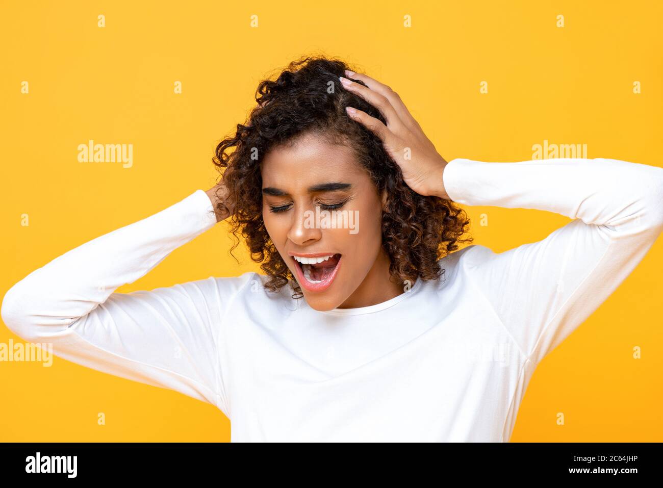 Close up portrait of confused African American woman  shouting while holding her head with both hands in isolated studio yellow background Stock Photo