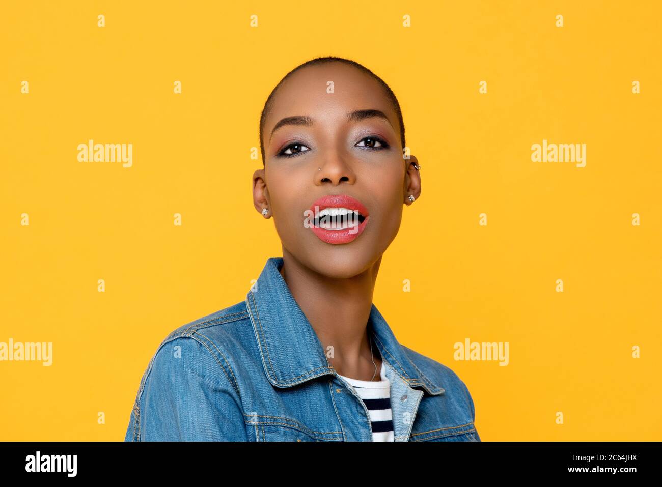 Close up beauty portrait of beautiful young African American woman looking at camera with mouth open isolated on studio yellow background Stock Photo