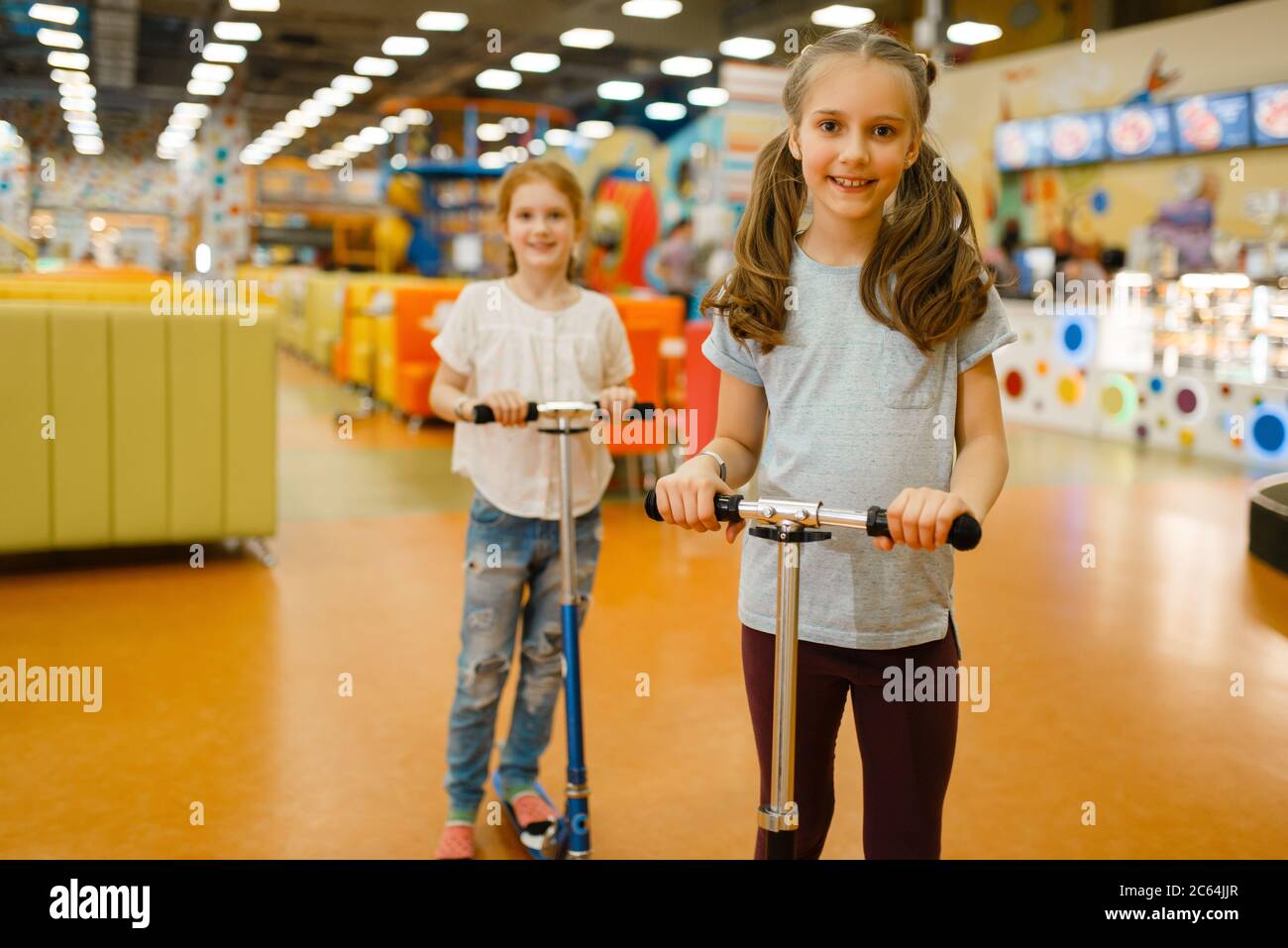 Little girlfriends rides on scooters, playground Stock Photo