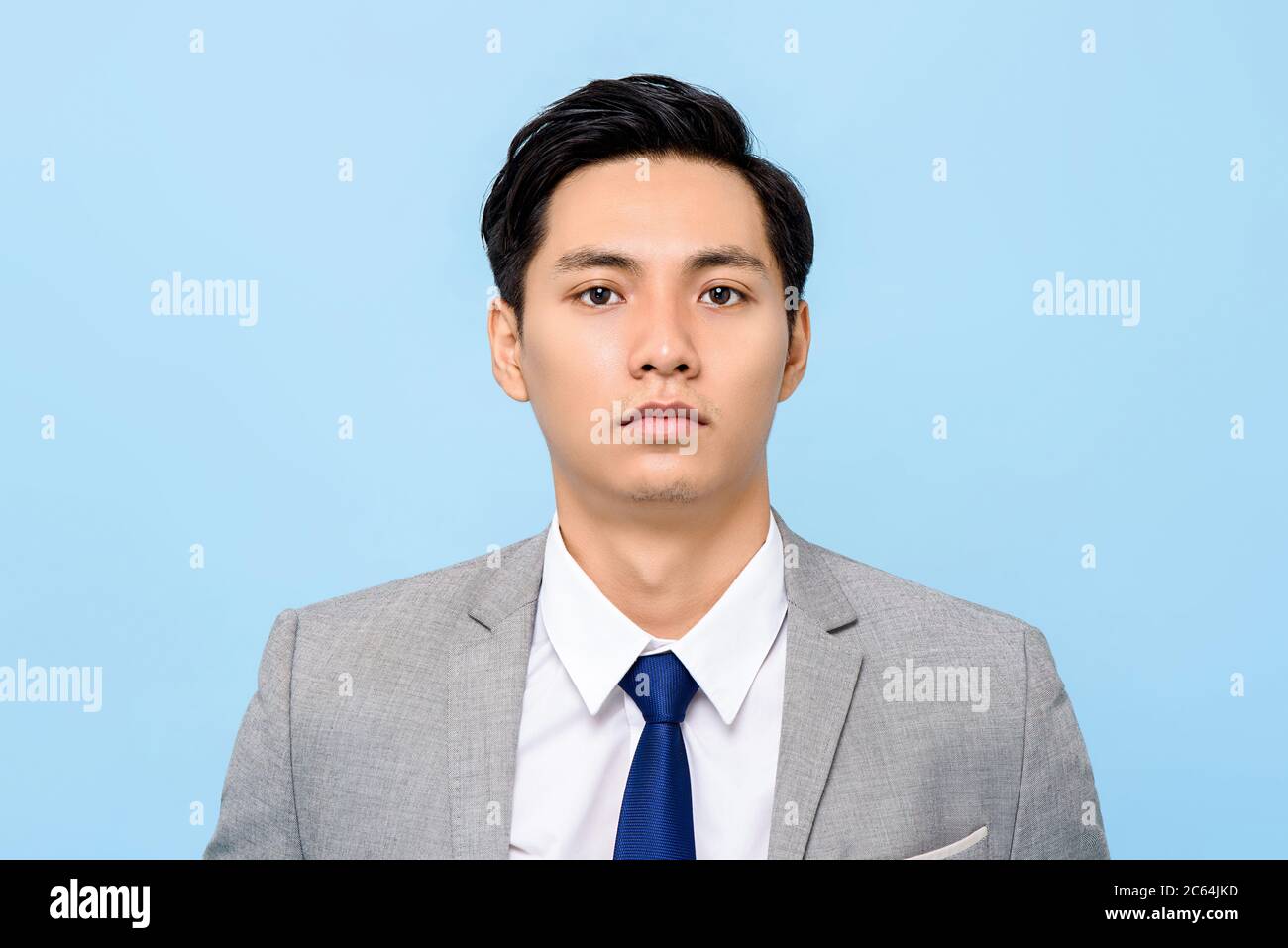 Close up portrait of serious young Asian businessman looking at camera in isolated studio blue background Stock Photo