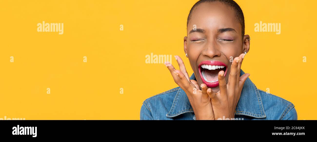 Panoramic close up portrait of ecstatic young African American woman screaming with hands covering mouth isolated studio yellow background Stock Photo