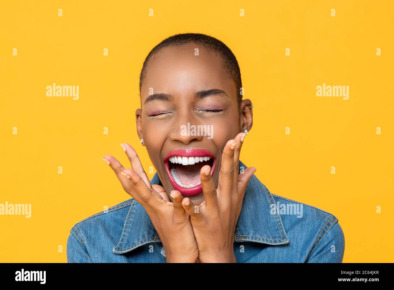 Close up portrait of ecstatic young African American woman screaming with hands covering mouth isolated on studio yellow background Stock Photo