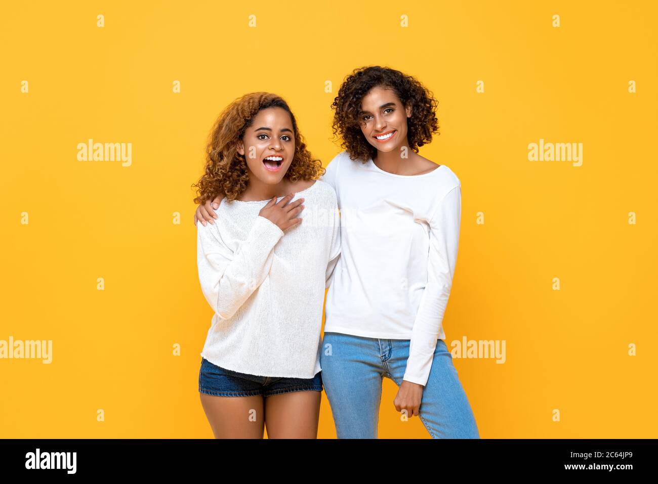 Portrait of two cheerful young African American women standing together while looking at camera in isolated studio yellow background Stock Photo