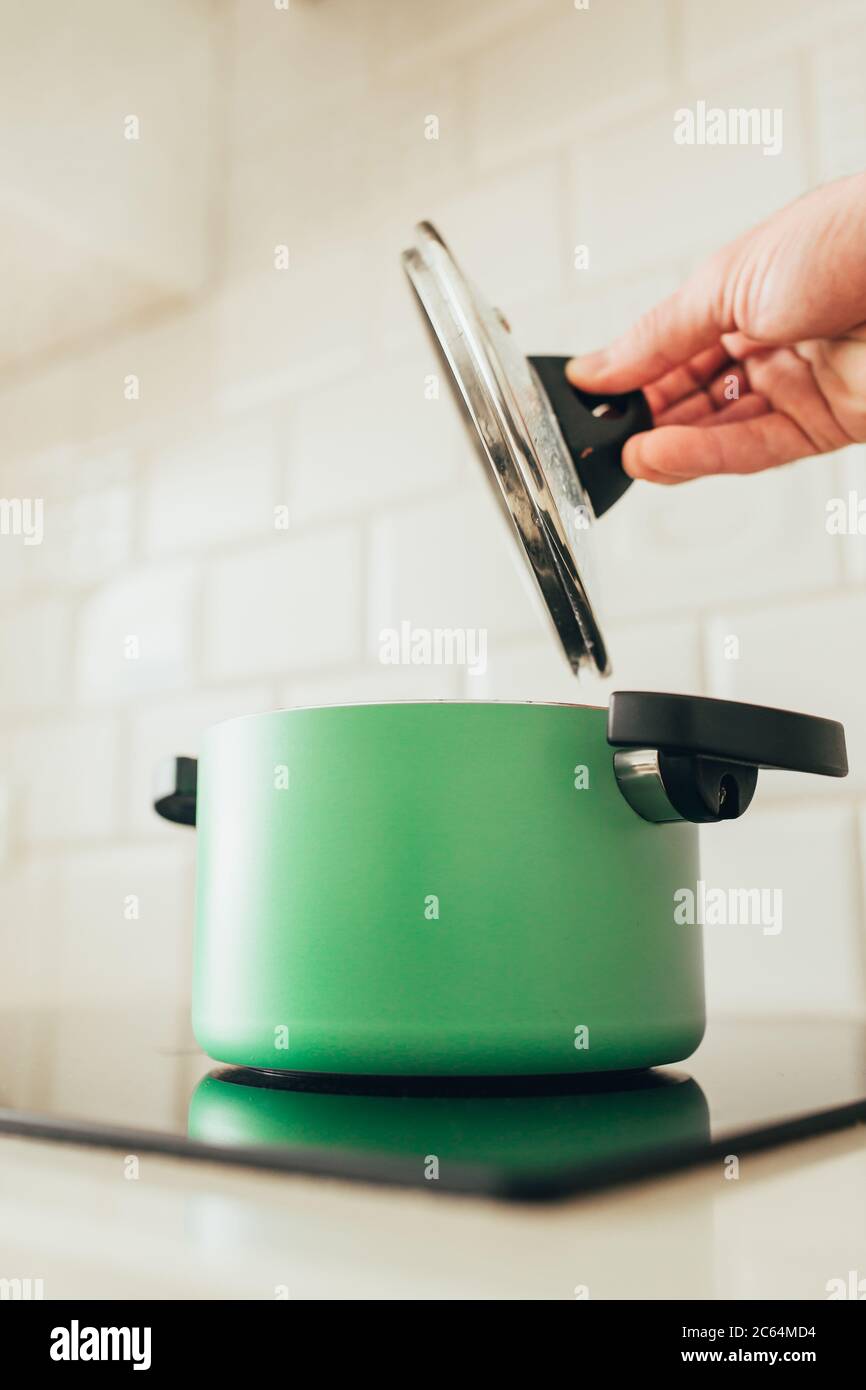 Green pan on induction cooker hand removes the lid Stock Photo Alamy