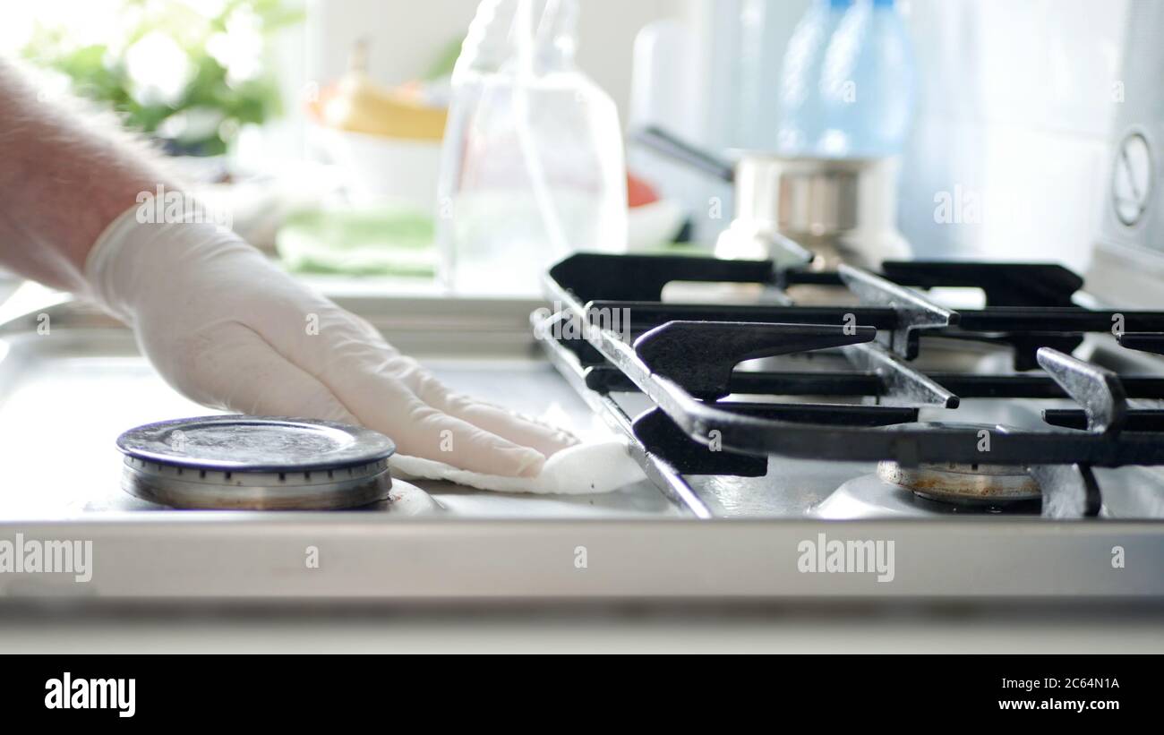 Busy Person in the Kitchen Wearing Gloves Cleans with Solution the Cooker Stove. Stock Photo