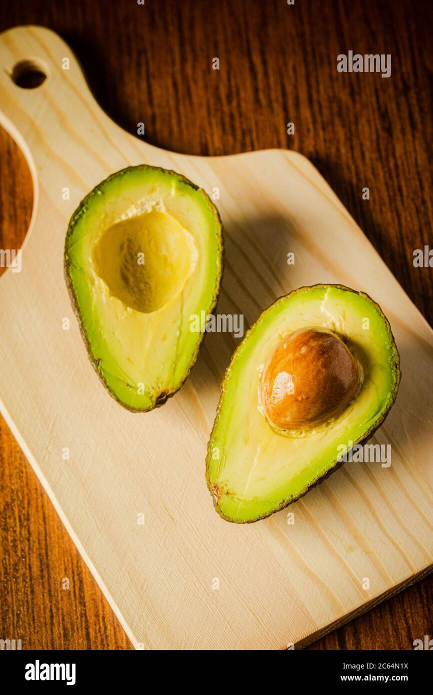 An avocado cut into half on a wooden cutting board with a dark background Stock Photo