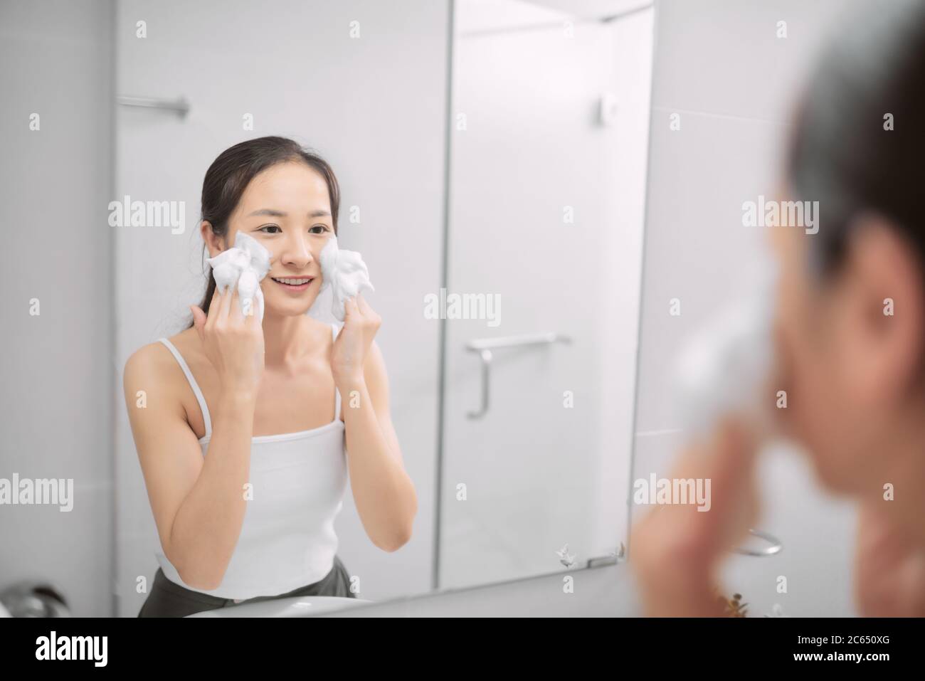 Skincare woman washing face in shower foaming face wash soap scrub on