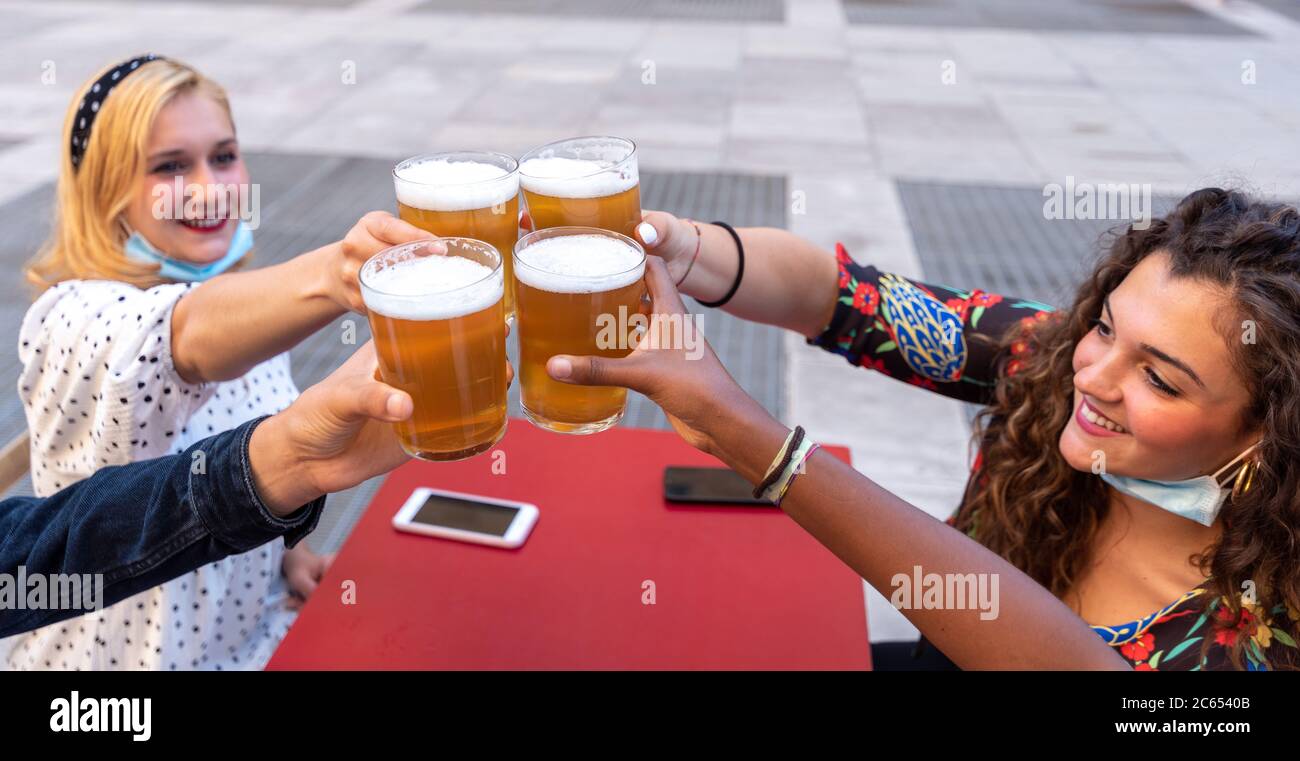 group of multi-ethnic friends toast raising glasses of beer, focus on the four raised beers and the hands of millenials toasting, blonde girl and curl Stock Photo