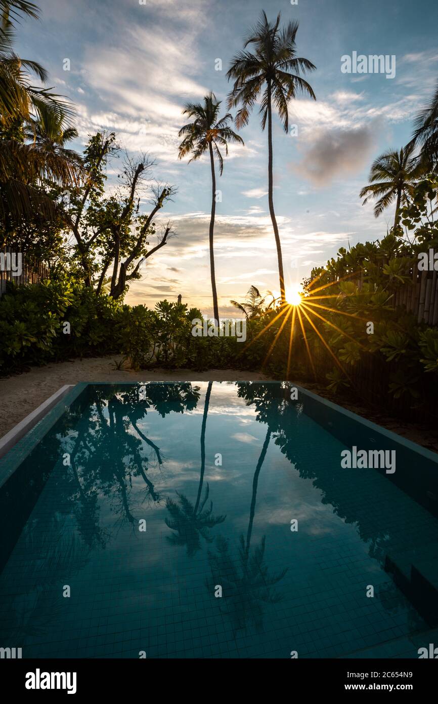 Cherish a sunset besides an infinity pool of island resorts in Maldives watching over the palm trees into the ocean horizon Stock Photo
