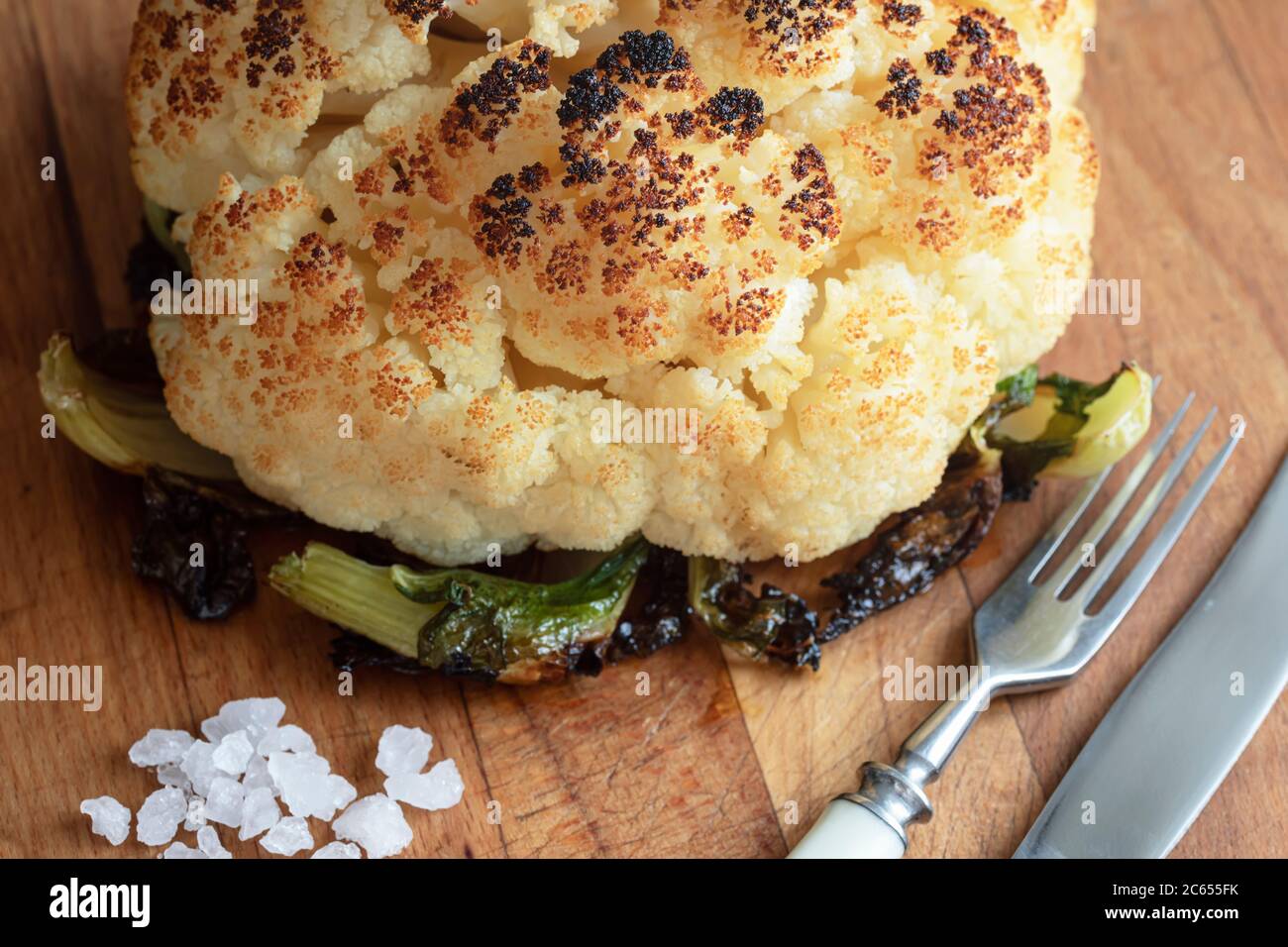 Whole grilled Cauliflower out of the oven with sea salt on a wooden board. Vegan food. Vegeterian food. Cooking at home. Close-up Stock Photo