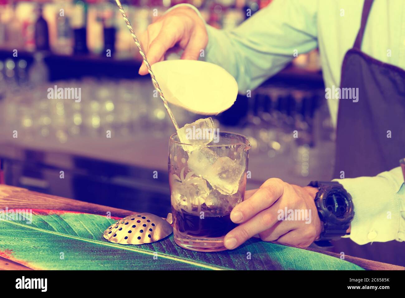 Bartender is adding ice cubes to the mixing glass, toned Stock Photo