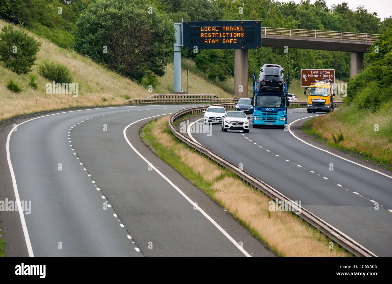 East Lothian, Scotland, United Kingdom, 7th July 2020. Covid-19 new message on A1 gantry: the third version of the pandemic message appears on overhead gantry near Haddington which reads 'Local Travel Restrictions Stay Safe' as Scotland eases into Phase 3 expected next week. The traffic on the dual carriageway is much heavier than has been apparent in recent months Stock Photo