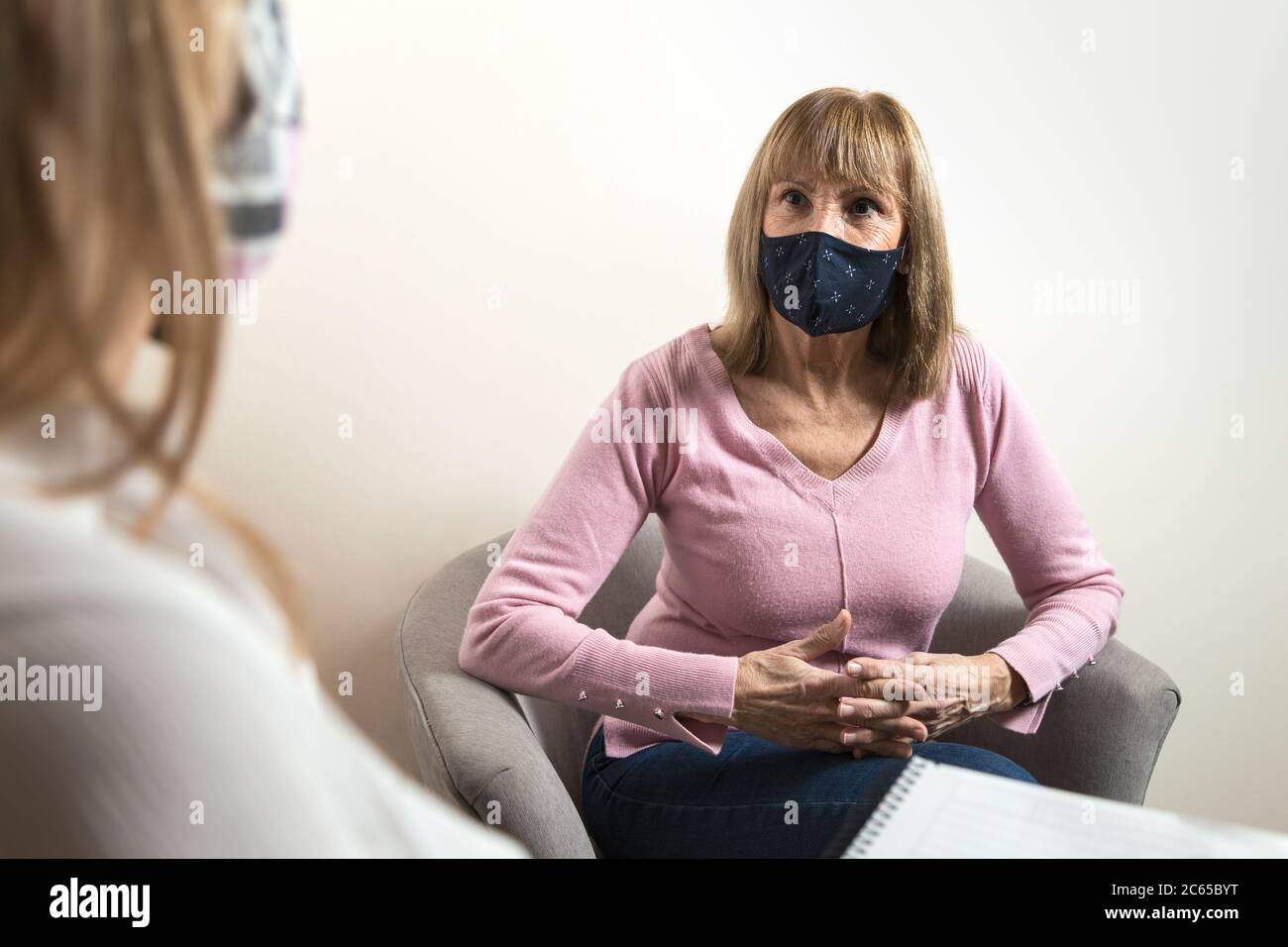 Woman with a chinstrap talking to another. Both with medical masks. Attention protocol. Worried woman being cared for by her therapist Stock Photo