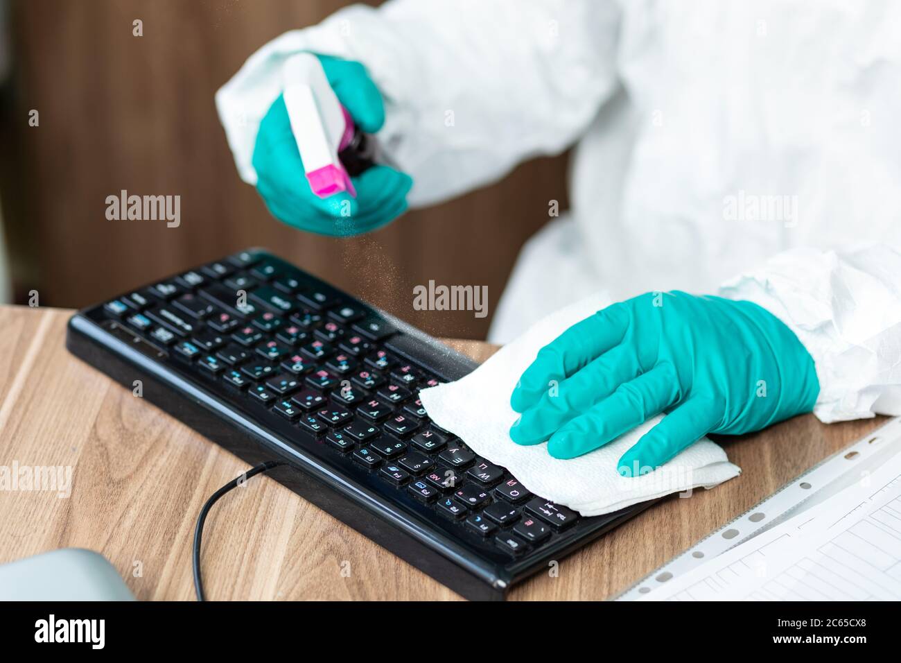Disinfection man with special white suite cleaning a PC computer with