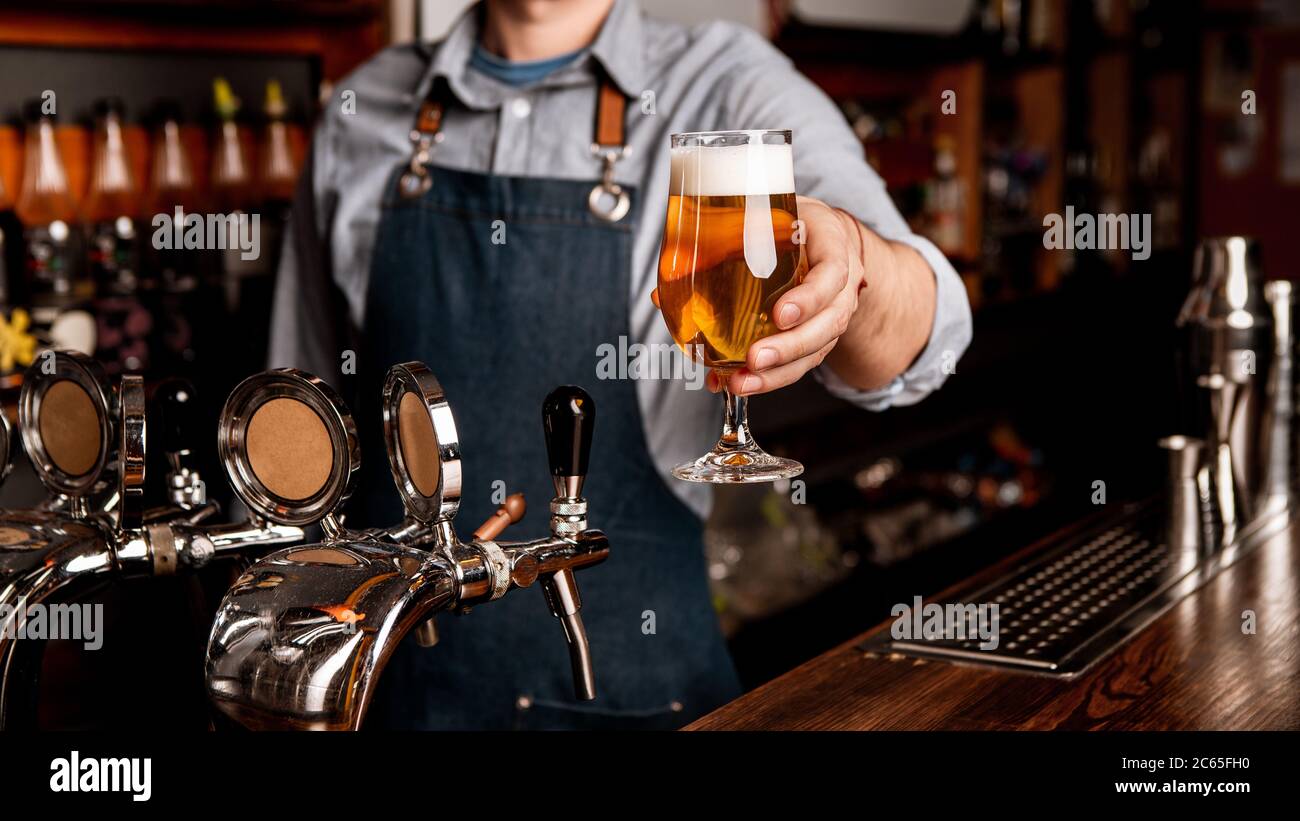 Fresh beer from keg. Glass of light lager with foam in hands of bartender in apron Stock Photo