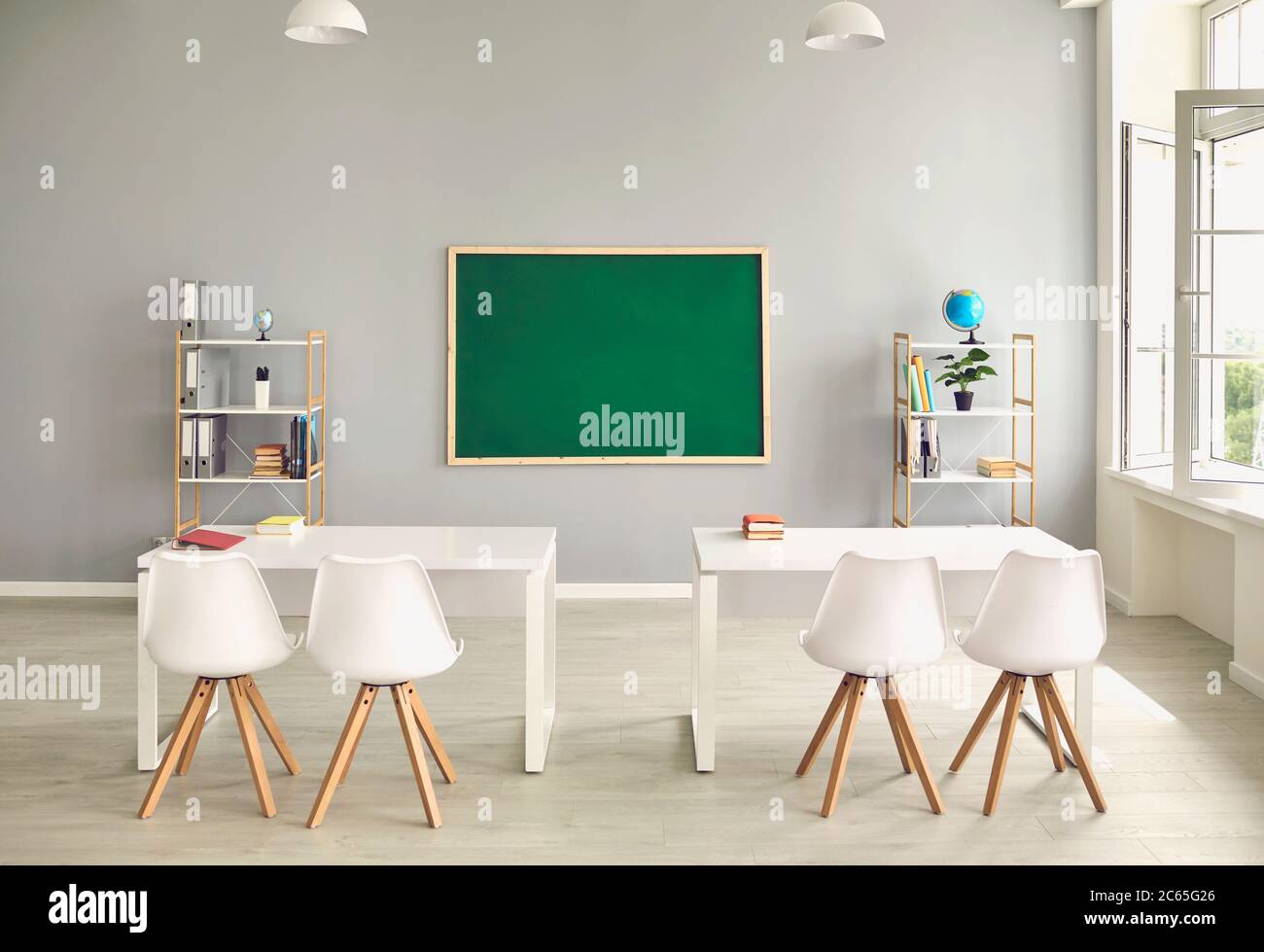 Empty school classroom interior with desks and chairs, space for text on chalkboard. Modern schoolroom with furniture Stock Photo