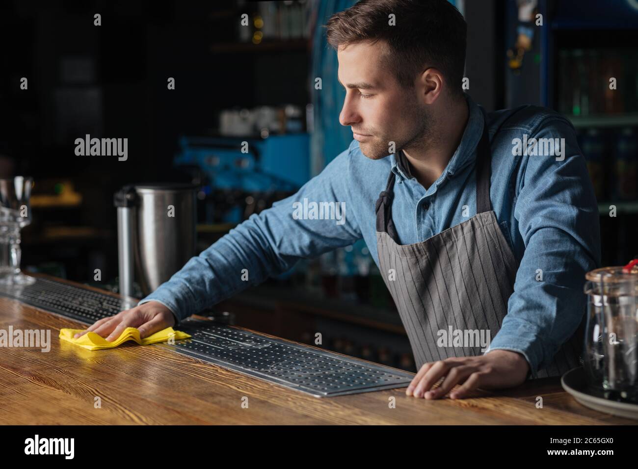 Cleanliness in pub. Professional bartender standing at counter, wiping wooden surface with rag Stock Photo