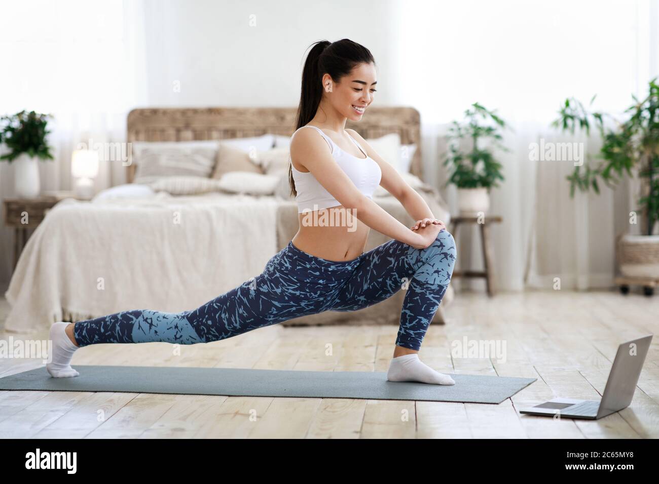 Home Training. Asian Girl Doing Stretching Exercises In Front Of Laptop Stock Photo