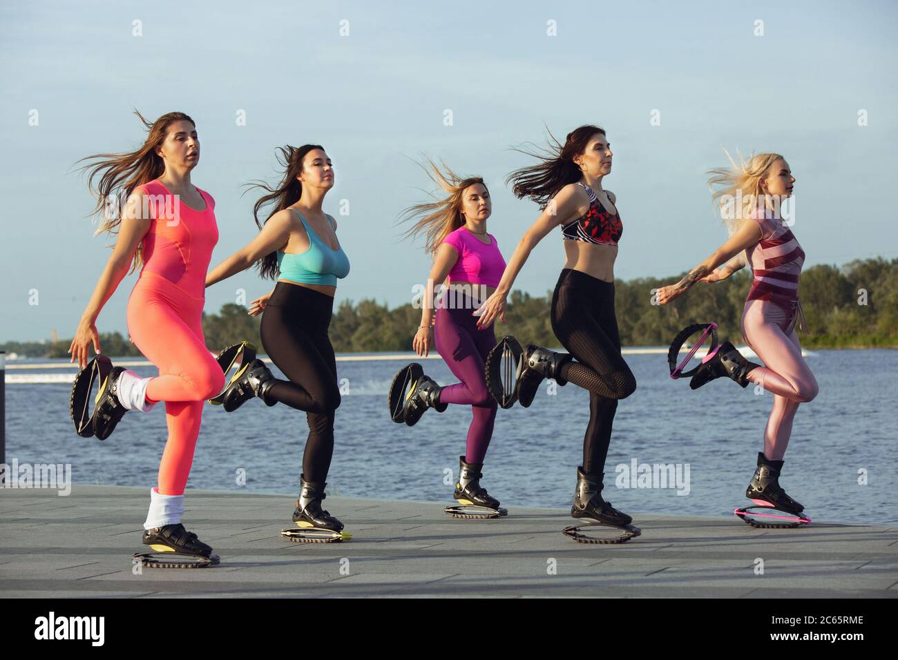 Beautiful women in sportswear jumping in a kangoo jumps shoes at the street  on summer's sunny day. Jumping high, active movement, action, fitness and  wellness. Fit female models during training Stock Photo 