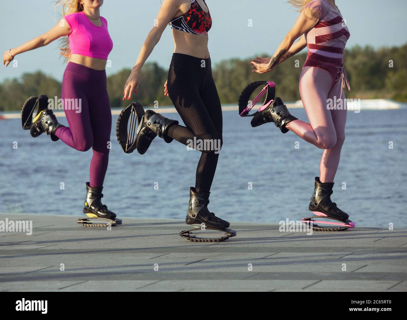 Close up women in sportswear jumping in a kangoo jumps shoes at the street  on summer's sunny day. Jumping high, active movement, action, fitness and  wellness. Fit female models during training Stock