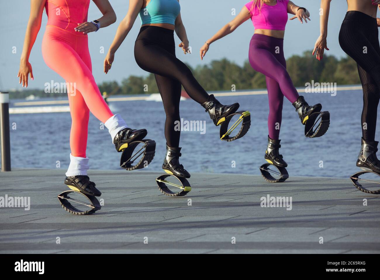 Beautiful women in sportswear jumping in a kangoo jumps shoes at the street  on summer's sunny day. Jumping high, active movement, action, fitness and  wellness. Fit female models during training Stock Photo -