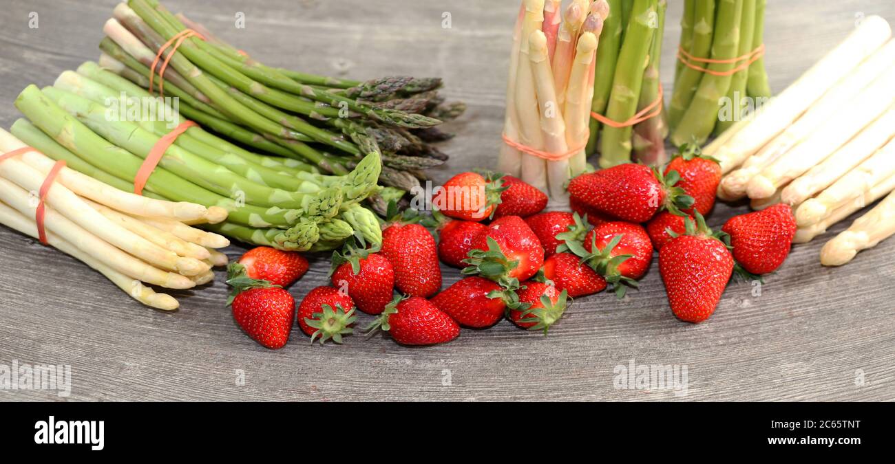 Grüne Spargel, weiße Spargel und frische Erdbeeren dekoriert auf einem rustikalen Holztisch Stock Photo