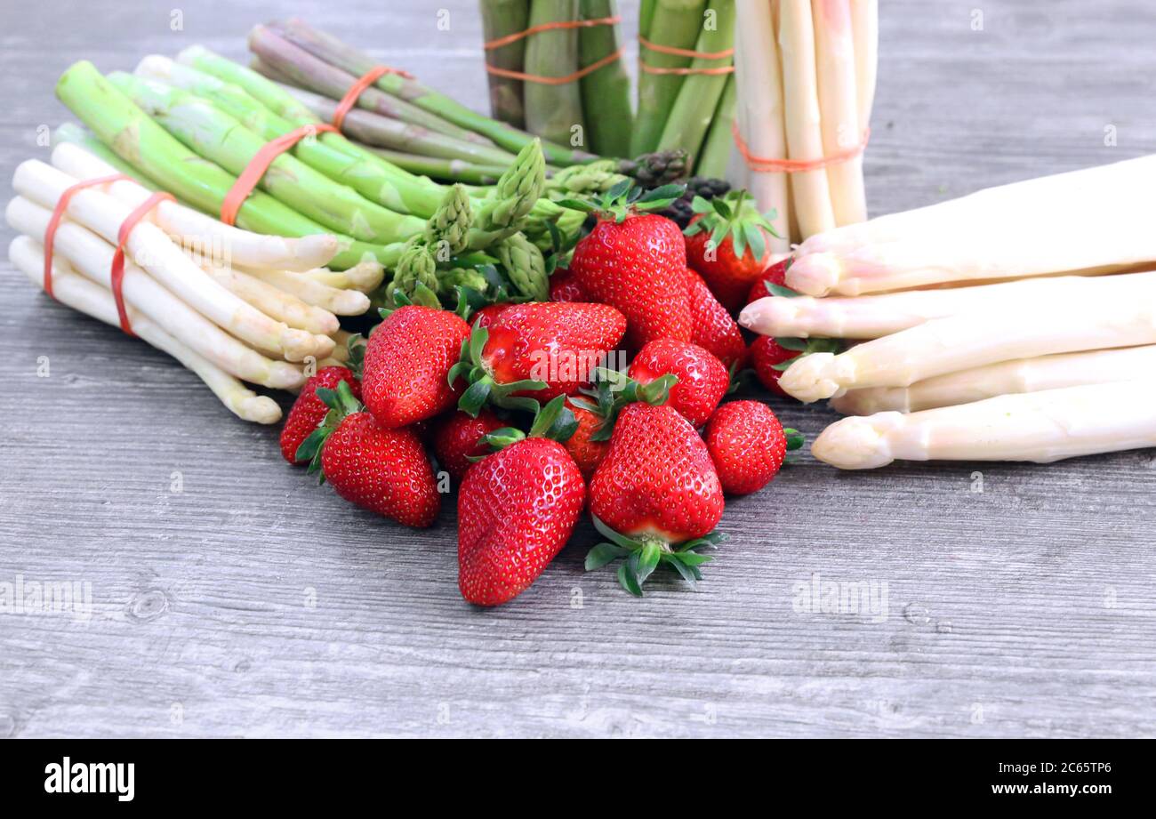 Grüne Spargel, weiße Spargel und frische Erdbeeren dekoriert auf einem rustikalen Holztisch Stock Photo