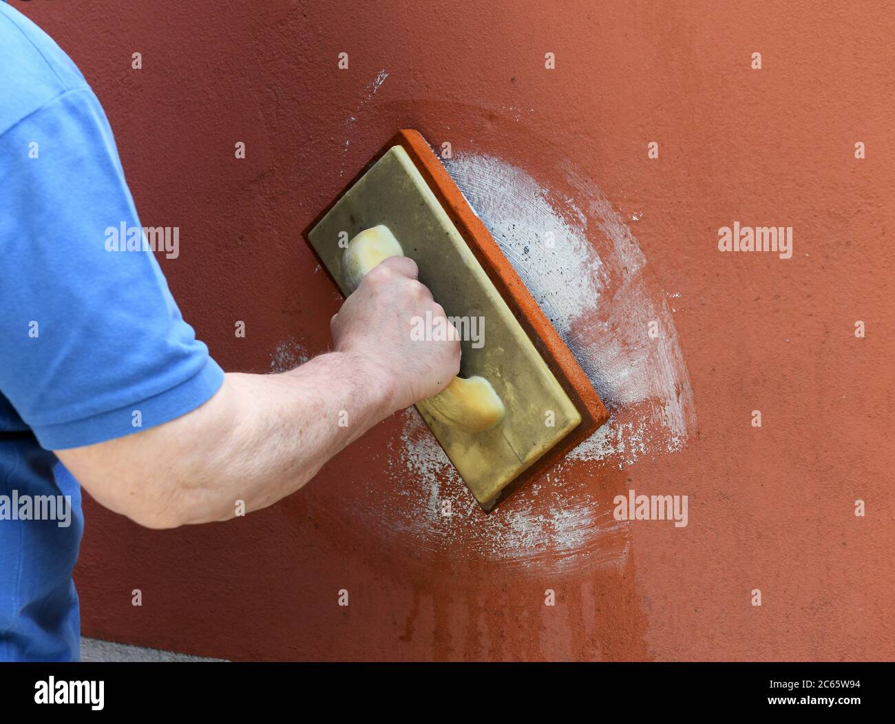 Bricklayer grouting masonry on a colored wall in a close up on his hand as he applies the grout in a maintenance, construction or renovation concept Stock Photo