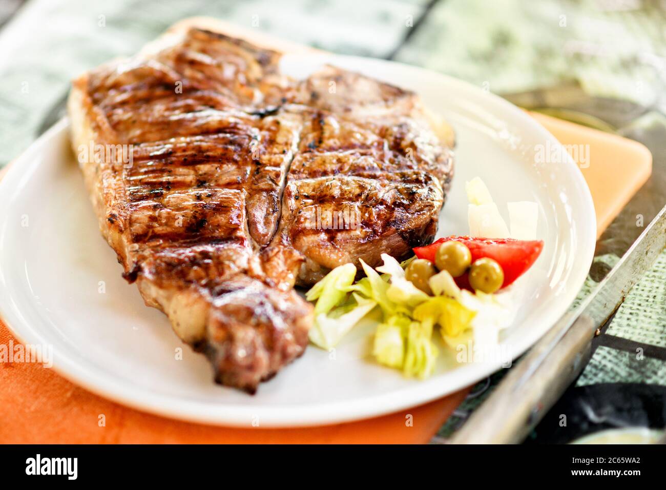 Grilled or barbecued Florentine steak on a plate served with fresh salad garnish in close up low angle with shallow dof Stock Photo