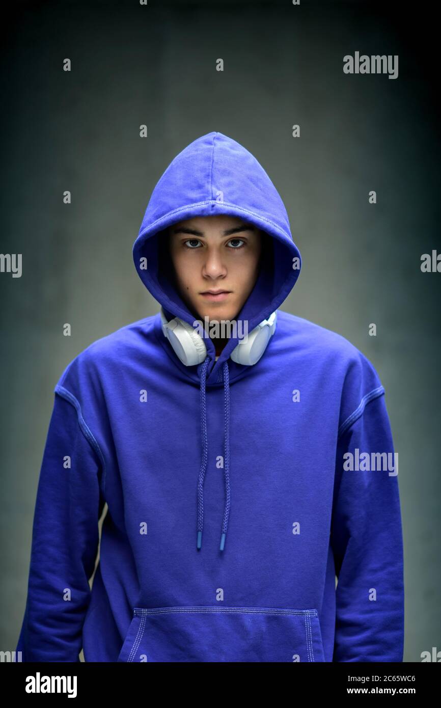 Moody serious teenage boy wearing a blue hoodie staring sullenly at the camera with earphones slung around his neck in a frontal portrait Stock Photo